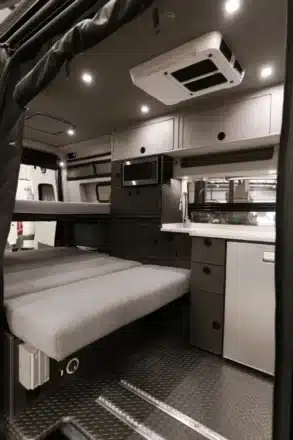 Innenraum eines ausgebauten Mercedes-Benz Sprinter Campervans mit Sitzbank, Küchenzeile, Mikrowelle und Oberschränken