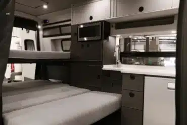 Innenraum eines ausgebauten Mercedes-Benz Sprinter Campervans mit Sitzbank, Küchenzeile, Mikrowelle und Oberschränken