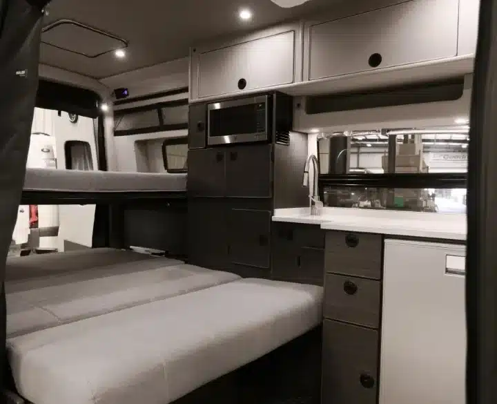 Innenraum eines ausgebauten Mercedes-Benz Sprinter Campervans mit Sitzbank, Küchenzeile, Mikrowelle und Oberschränken