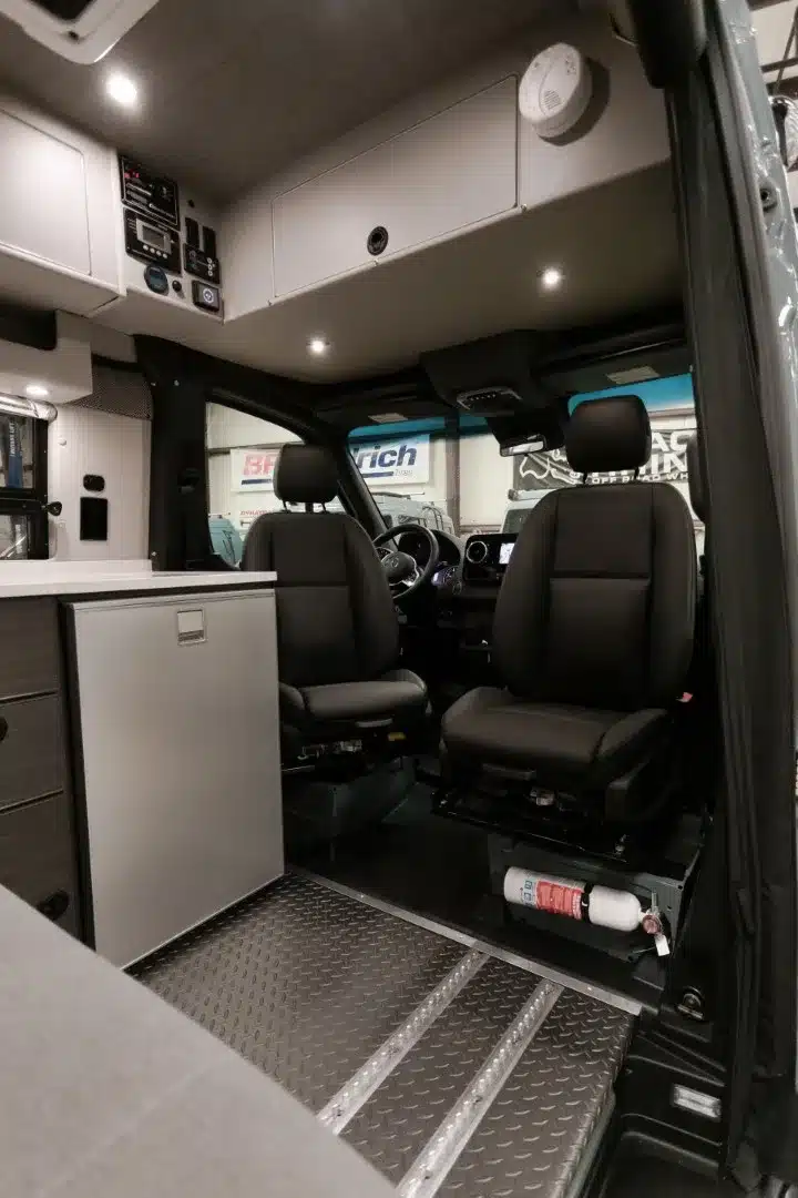 Innenraum eines ausgebauten Mercedes-Benz Sprinter Campervans mit Fahrerhaus, Küchenmodul und Oberschränken