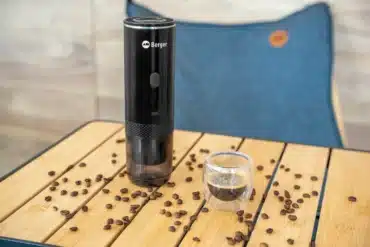 Schwarze tragbare Berger EspressoTime neben einer Tasse Espresso auf einem Holztisch