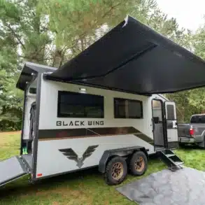 Black Wing 724-X Toy Hauler mit Heckrampe, Markise und Pick-up im Wald