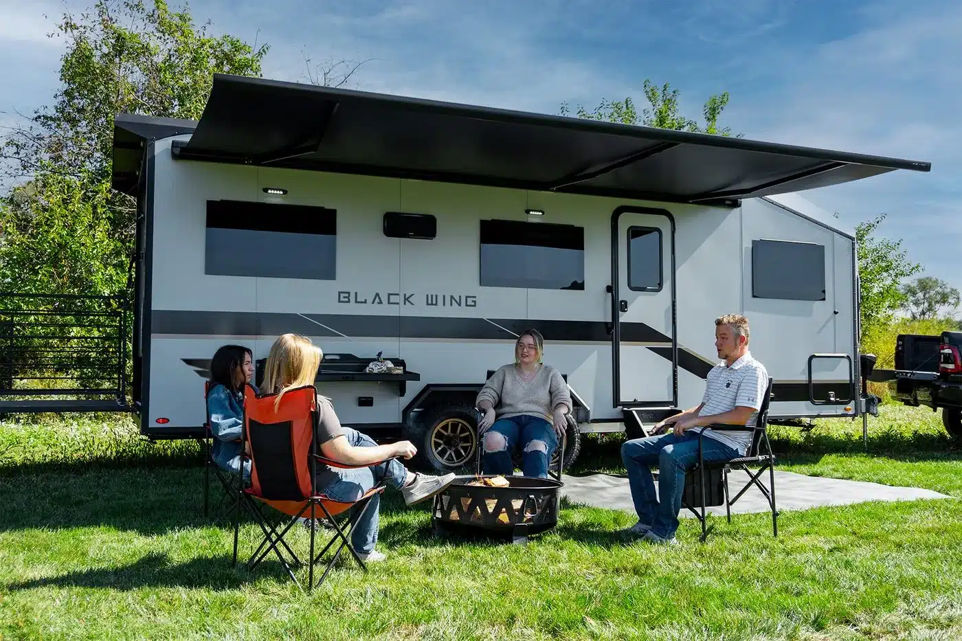Black Wing Toy Hauler mit ausgefahrener Markise und sitzenden Campern auf einer Wiese