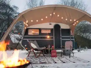 Schwarzer Constructam C190/B mit Vorzelt, Sitzmöbeln und Feuerstelle im Schnee