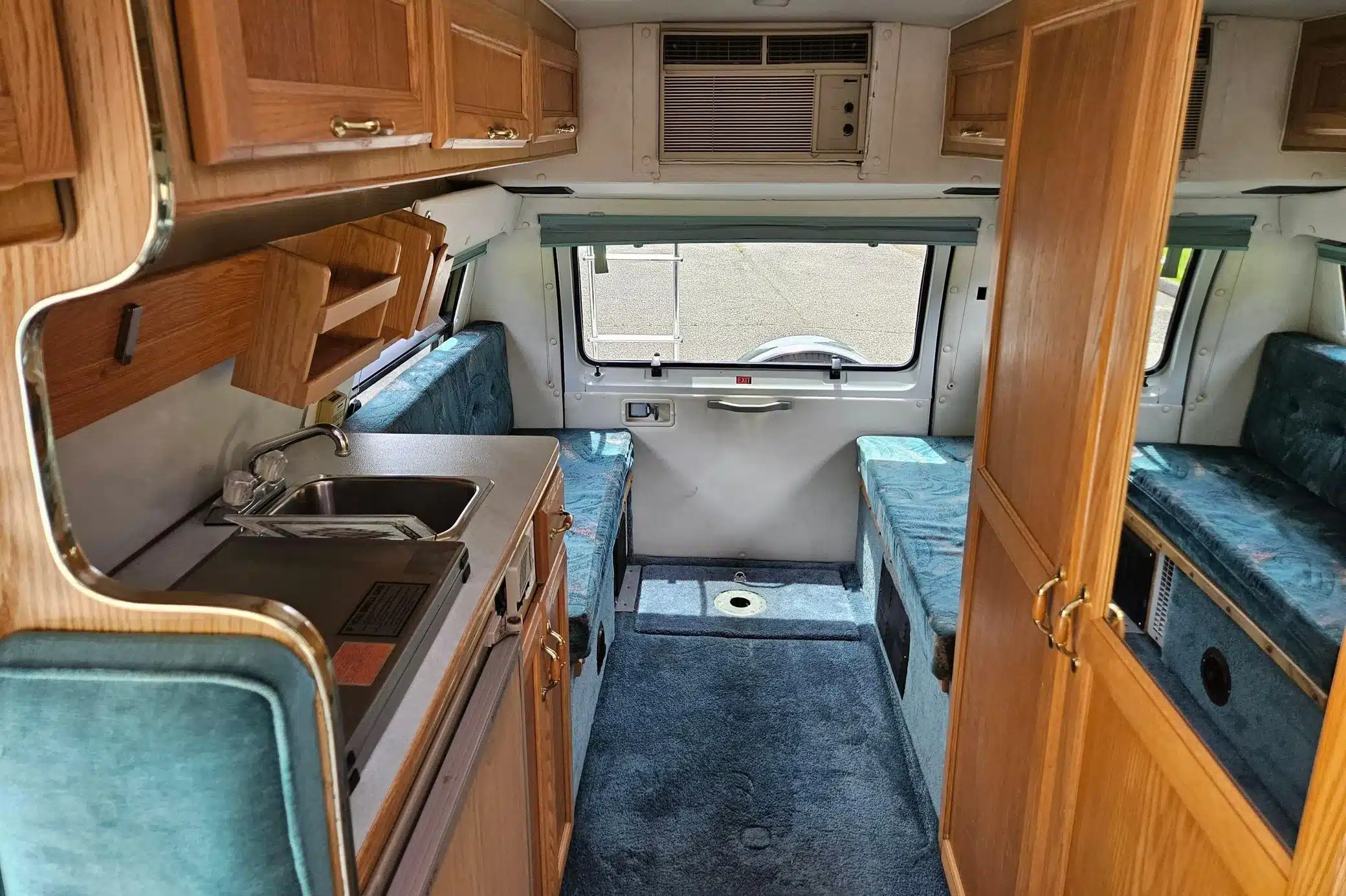 Innenraum eines Dodge Ram Van B350 Leisure Travel RV mit blauen Sitzpolstern, Holzschränken und Küchenzeile