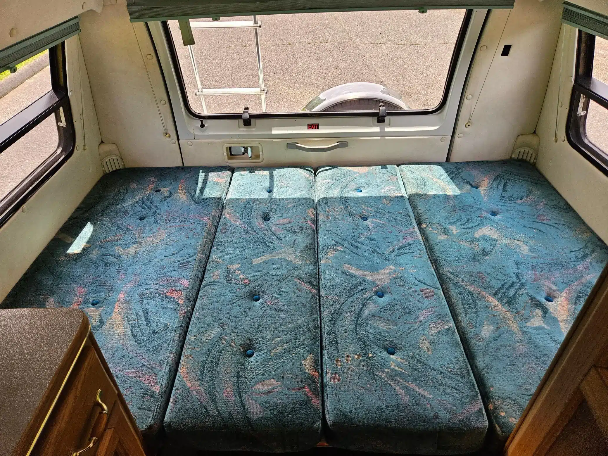 Ausgeklapptes Bett mit blauen Polstern im Innenraum eines Dodge Ram Van B350 Leisure Travel Wohnmobils