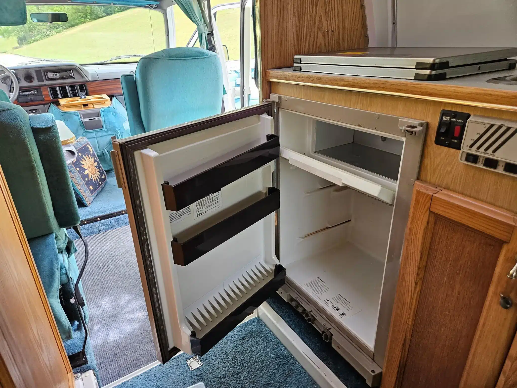 Blauer Innenraum eines Dodge Ram Van B350 Leisure Travel Wohnmobils mit Holzschränken, Cockpit und geöffneter Kühl-Gefrierkombination