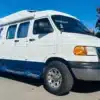 Weiß-blauer Dodge Ram Van B3500 Camper mit Hochdach und Markise auf einem Parkplatz