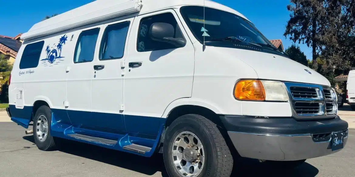 Weiß-blauer Dodge Ram Van B3500 Camper mit Hochdach und Markise auf einem Parkplatz