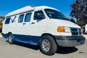 Weiß-blauer Dodge Ram Van B3500 Camper mit Hochdach und Markise auf einem Parkplatz