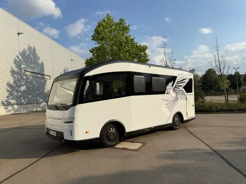 Weißer elektrischer EVOLVE-Reisemobil-Demonstrator mit schwarzer Fensterfront und Vogelgrafik vor einem Messegebäude
