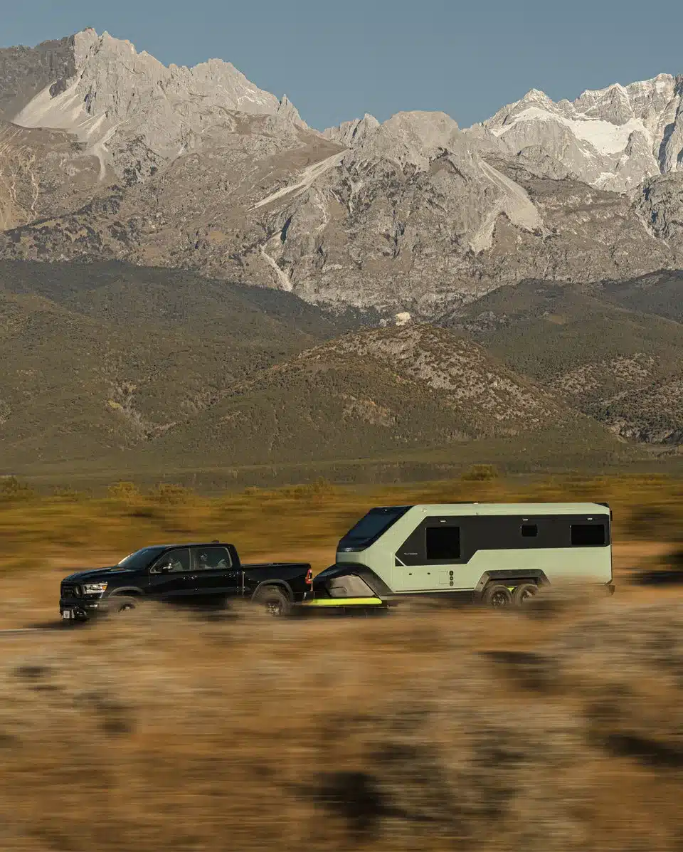 Evotrex PG5 Wohnanhänger hinter einem schwarzen Pick-up vor einer Berglandschaft