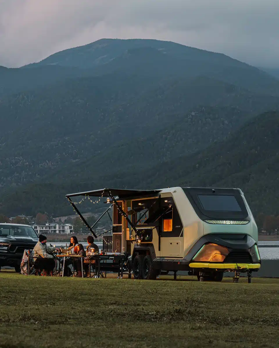 Evotrex PG5 Wohnanhänger mit ausgeklappter Heckterrasse und Sitzgruppe vor einer Bergkulisse
