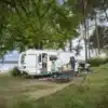 Weißer Fendt-Caravan BIANCO mit Familie und Campingmöbeln an einem See im Wald