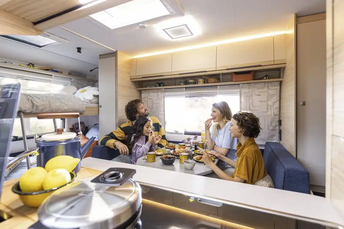 Heller Innenraum eines Fendt-Caravan BIANCO mit Familie an der Sitzgruppe, Küche und Schlafbereich
