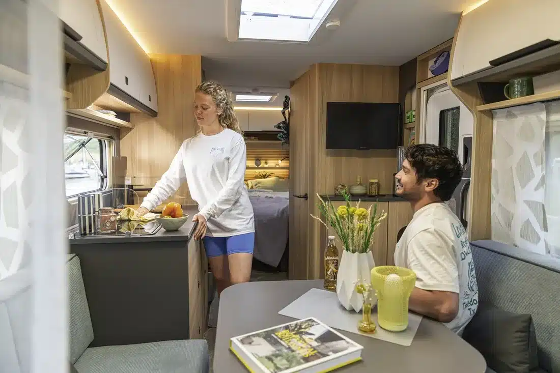 Innenraum eines Fendt-Caravan APERO mit Küche, Sitzgruppe, Schlafbereich und zwei Personen