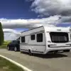 Weißer Fendt-Caravan DIAMANT Wohnwagen mit schwarzem Pkw auf einer Landstraße