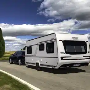 Weißer Fendt-Caravan DIAMANT Wohnwagen mit schwarzem Pkw auf einer Landstraße