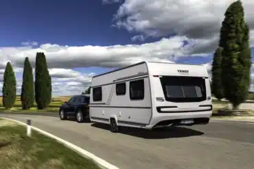 Weißer Fendt-Caravan DIAMANT Wohnwagen mit schwarzem Pkw auf einer Landstraße