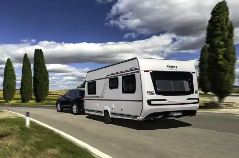 Weißer Fendt-Caravan DIAMANT Wohnwagen mit schwarzem Pkw auf einer Landstraße