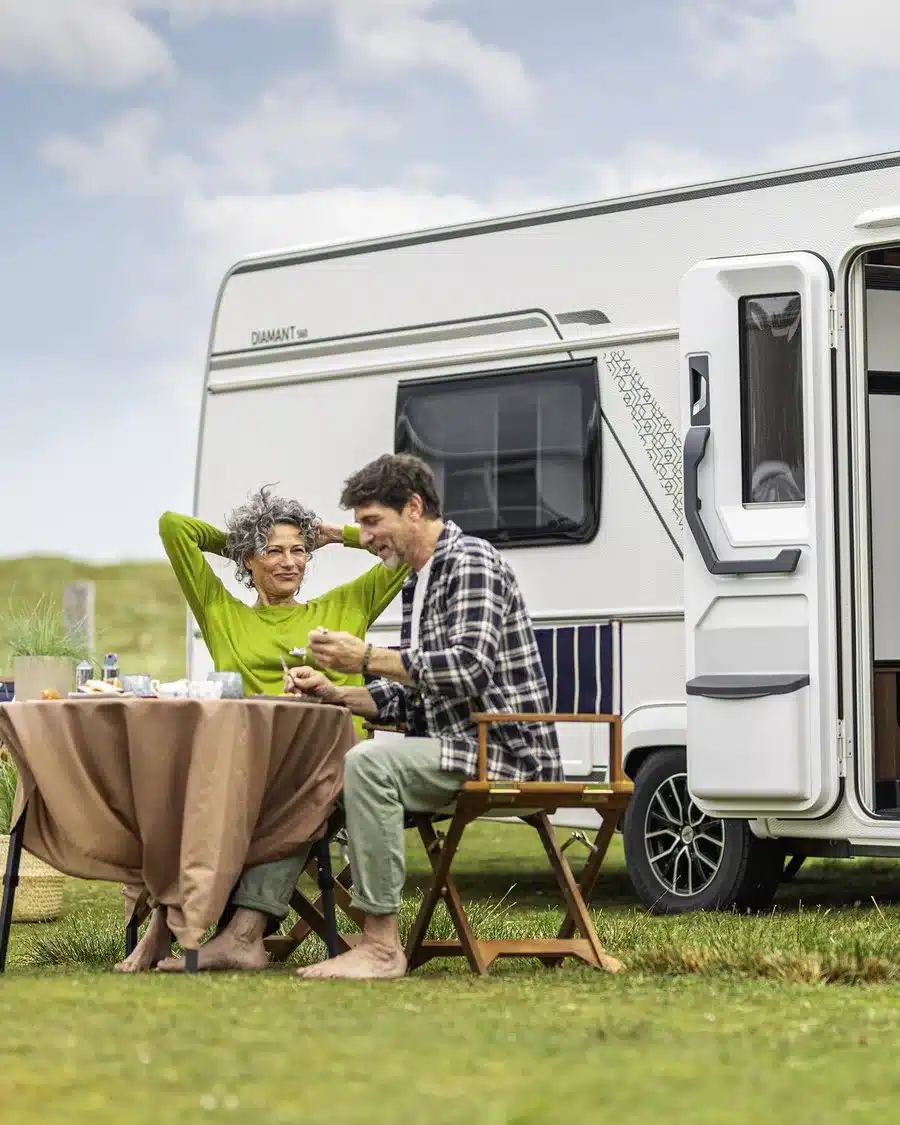 Fendt-Caravan DIAMANT 560 mit geöffneter Tür und einem Paar beim Essen auf einem Campingplatz
