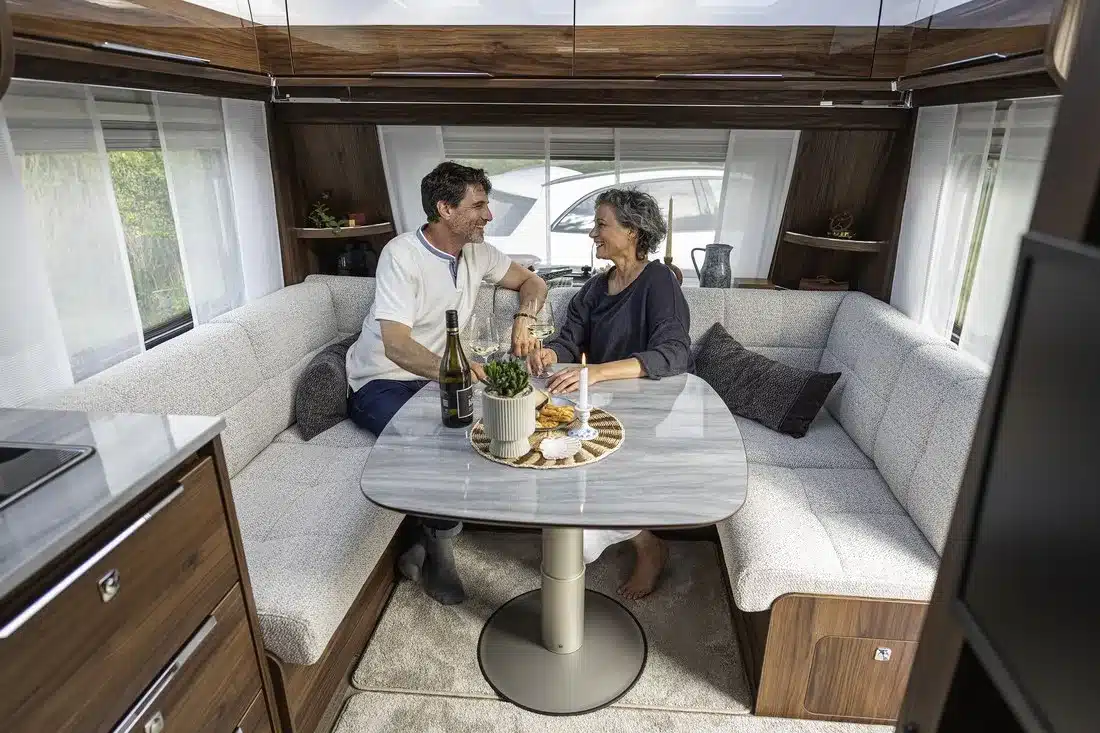 Innenraum eines Fendt-Caravan DIAMANT mit großer Rundsitzgruppe, Tisch und zwei Personen