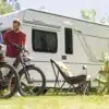 Weißer Fendt-Caravan TENDENZA 465 mit zwei Fahrrädern, Campingstühlen und Tisch auf einer Wiese.