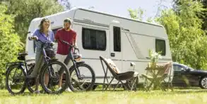 Weißer Fendt-Caravan TENDENZA 465 mit zwei Fahrrädern, Campingstühlen und Tisch auf einer Wiese.