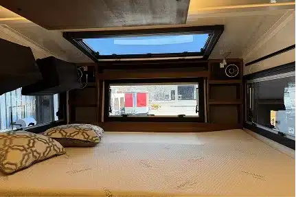 Queensize-Bett im Innenraum des Field Adventure Vehicle mit Dachfenster, Seitenfenstern und Holzverkleidung