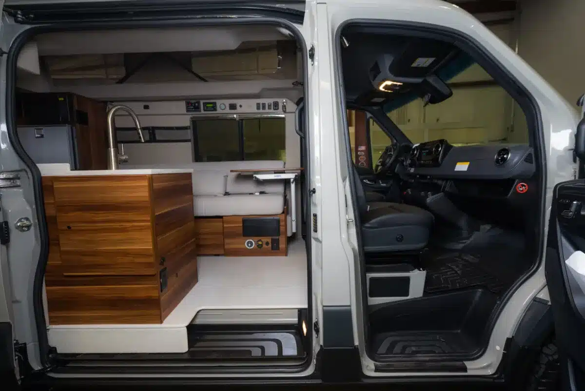 Innenraum eines Field Van Campervans mit Holzküche, Spüle, Sitzbank und offenem Durchgang zum Fahrerhaus