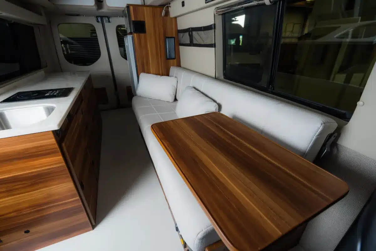 Innenraum eines Field Van Canyon Campervans mit weißer Sitzgruppe, Holztisch und Küchenzeile