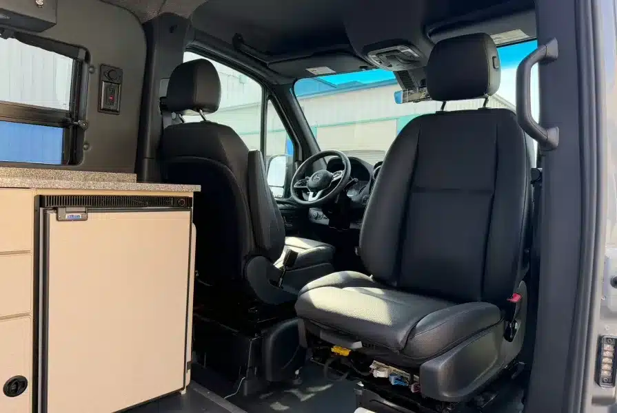 Innenraum eines Campervans mit Fahrerhaus, drehbarem Beifahrersitz und Küchenmodul mit Kühlschrank