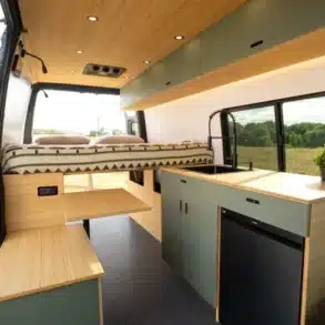Innenraum des Flatiron Camper Vans mit Bett, Küchenzeile, Sitzbank und Holzverkleidung