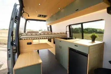 Innenraum des Flatiron Camper Vans mit Bett, Küchenzeile, Sitzbank und Holzverkleidung