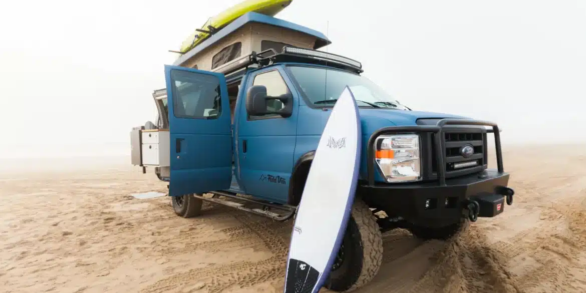 Blauer Field Van Ford Classic 4x4 mit Dachzelt, Surfbrett und Offroad-Stoßfänger auf Sand