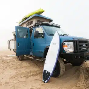 Blauer Field Van Ford Classic 4x4 mit Dachzelt, Surfbrett und Offroad-Stoßfänger auf Sand