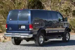 Dunkelblauer Ford E-350 Quigley 4x4 Campervan in einer Waldlandschaft
