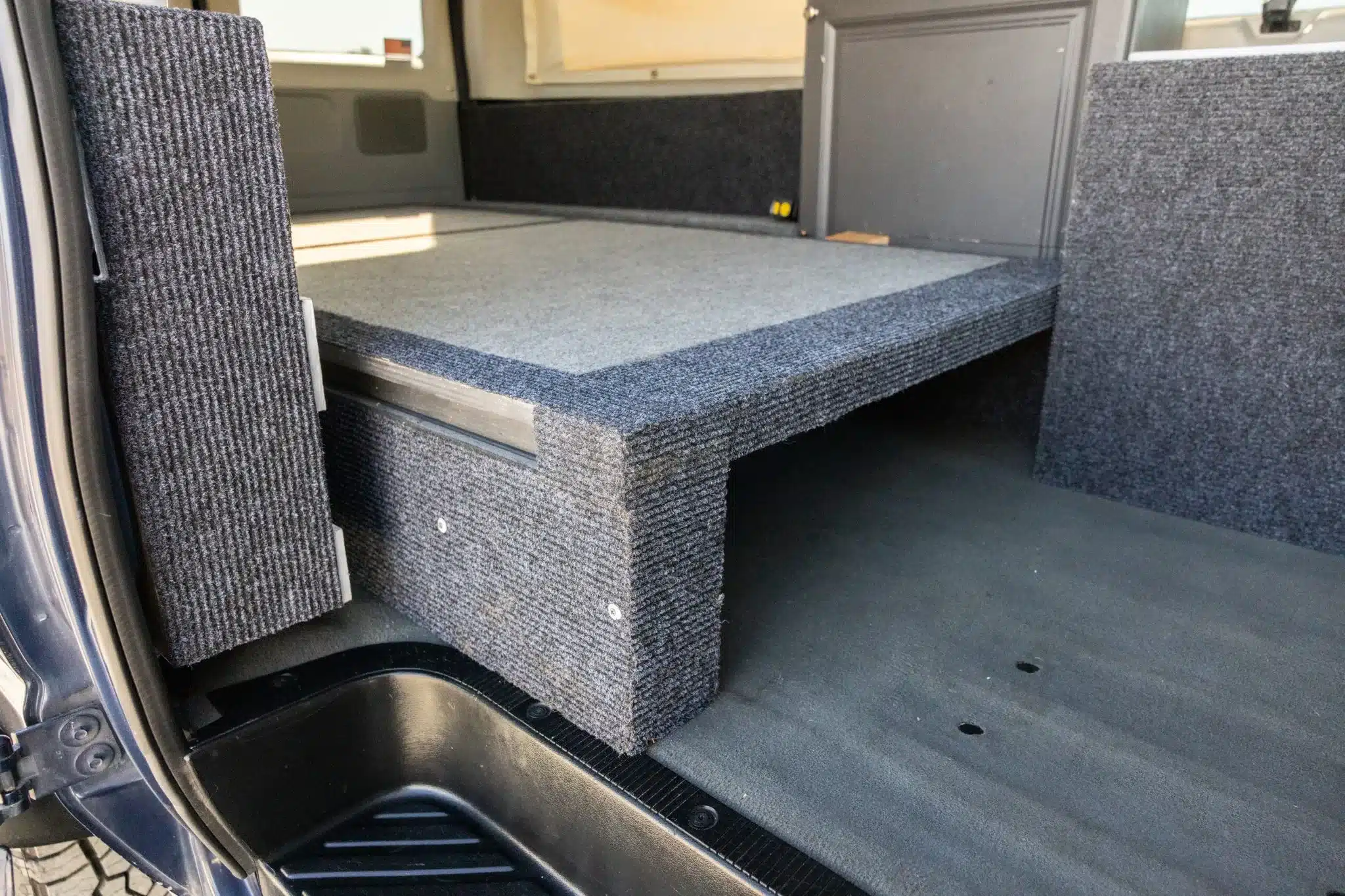 Innenraum des Ford E-350 mit grauer Schlafplattform und Camperausbau