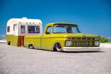 Grüner klassischer Ford F-100 mit weißem Stoßfänger und maßgefertigtem zweifarbigem Reiseanhänger