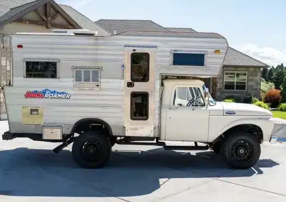 Weißer klassischer Ford F-350 Pickup mit silberner Wohnkabine vor einem Wohnhaus
