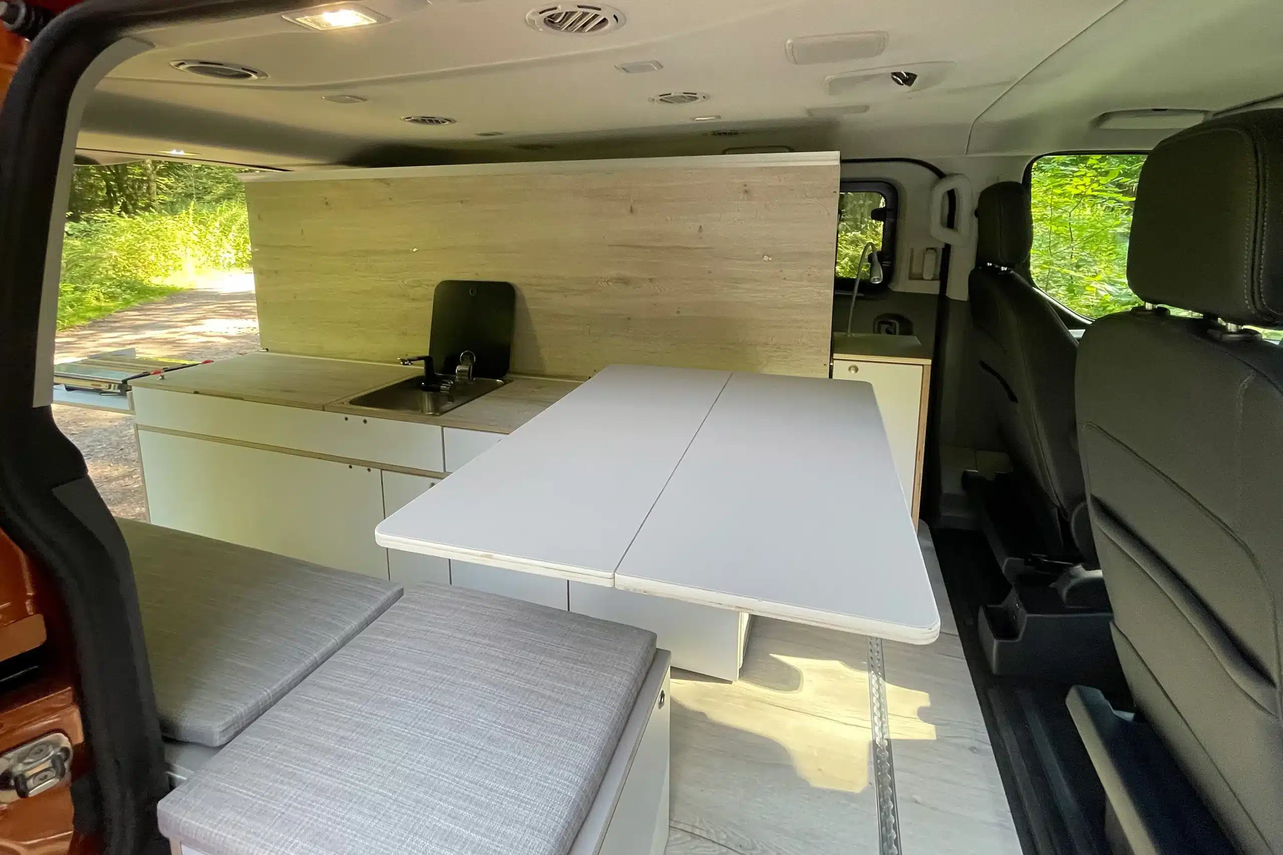 Innenraum eines Ford Transit Campervans mit Good Life Campermodul, Küche, Sitzbank und Bett