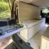 Innenraum eines Ford Transit Campervans mit Küchenmodul, Gaskocher, Stauraum und Sitzbank