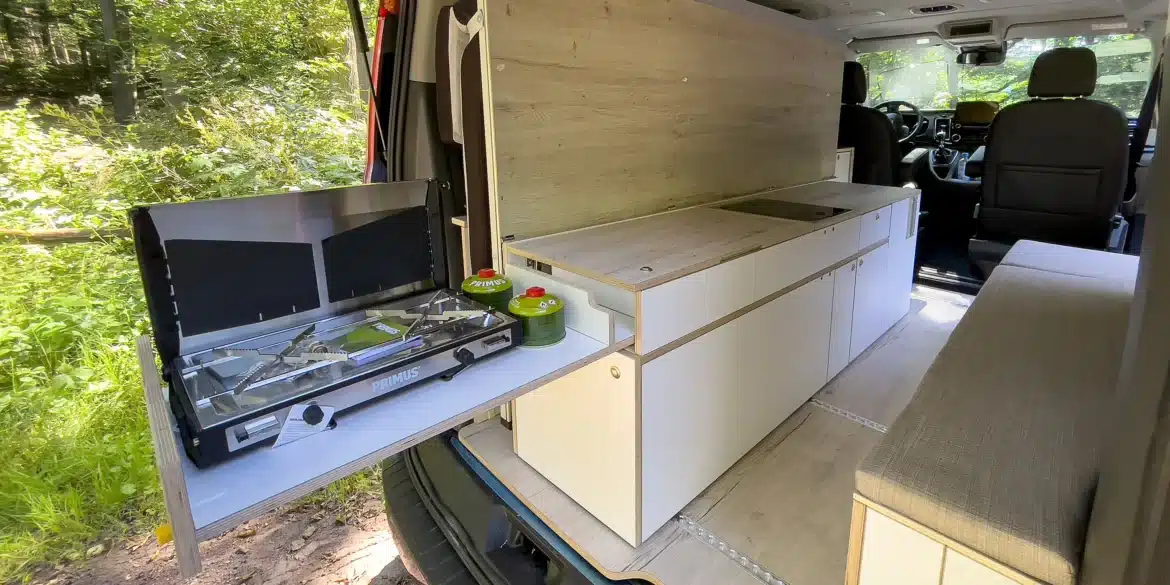 Innenraum eines Ford Transit Campervans mit Küchenmodul, Gaskocher, Stauraum und Sitzbank