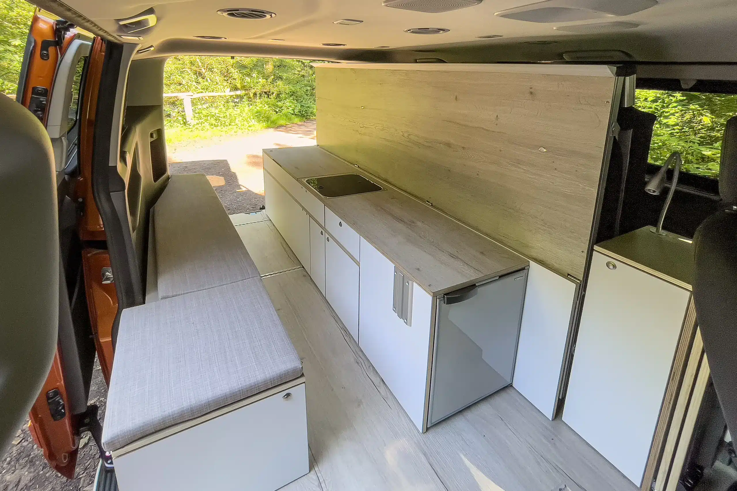 Innenraum eines zum Camper umgebauten Ford Transit mit Sitzbank, Küchenzeile und Stauraum