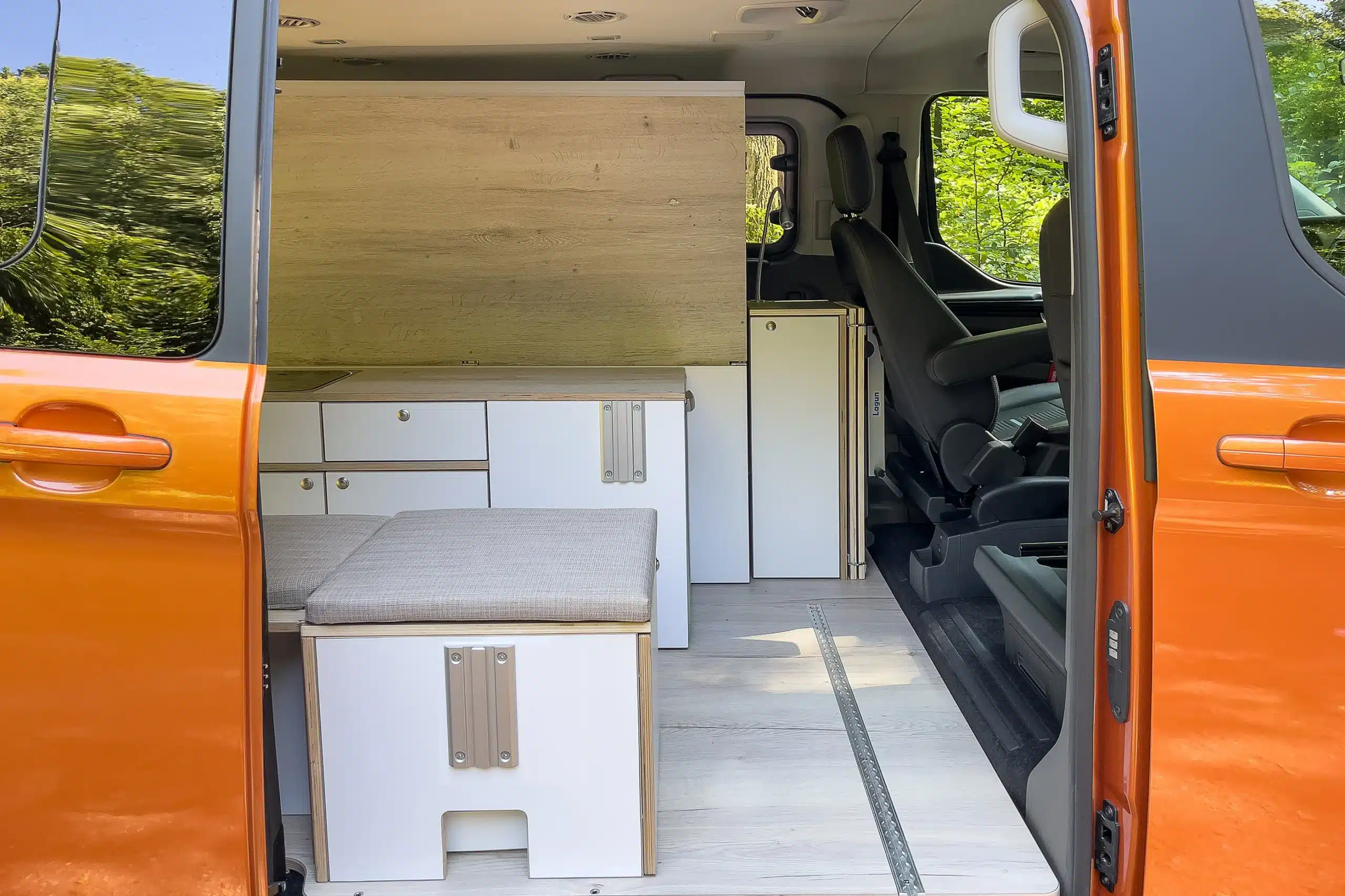 Innenraum eines orangefarbenen Ford Transit Campervans mit Good Life Campermodul, Bett und Küchenmöbeln