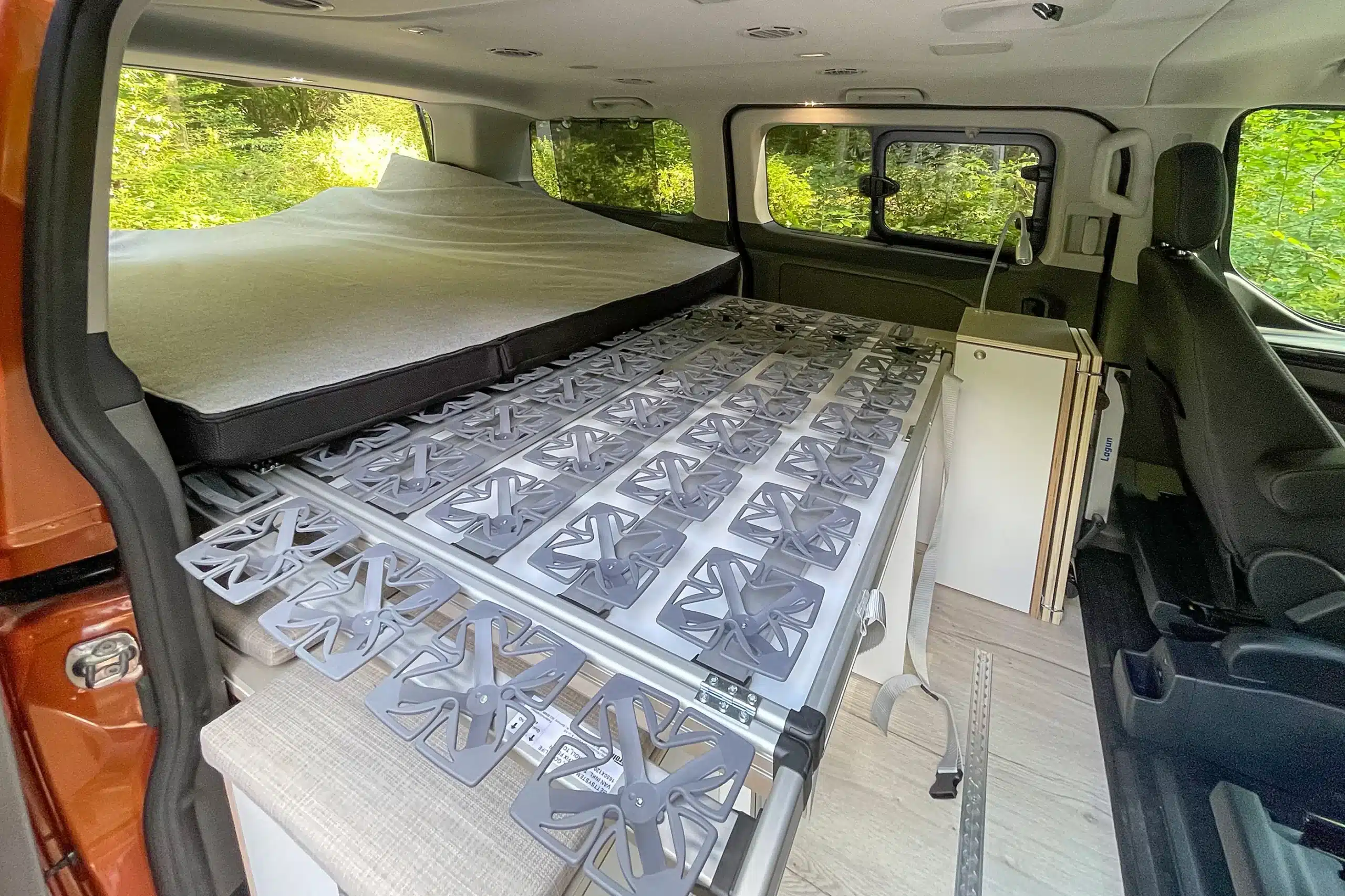 Innenraum eines Ford Transit Campervans mit Bett, Küchenmodul und modularer Bodenplatte