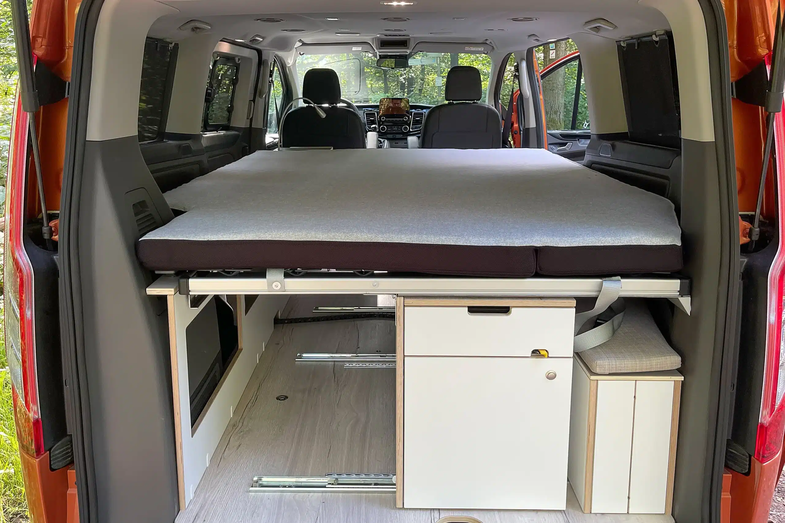 Innenraum eines Ford Transit Campervans mit Bettfläche, Küchenmöbeln und Stauraum