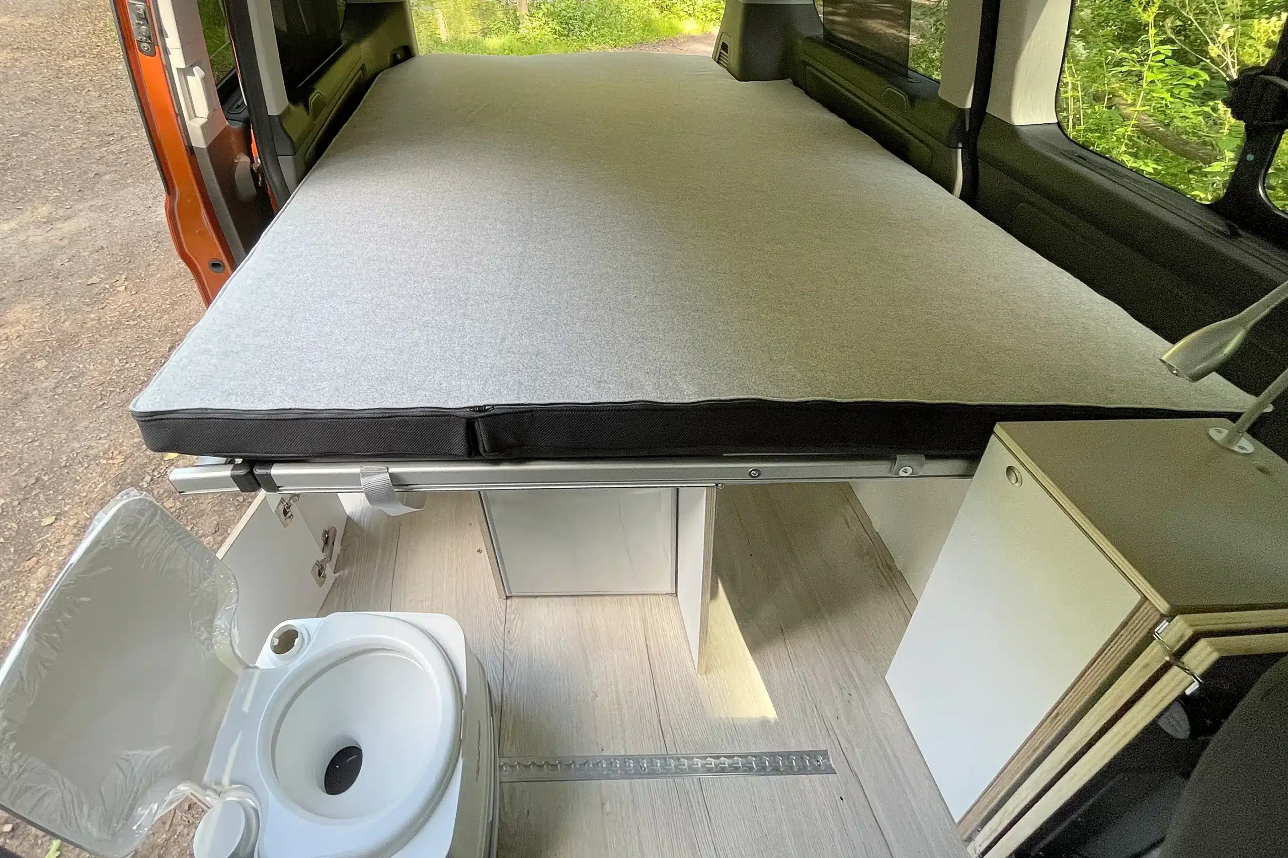 Innenraum eines Ford Transit Campers mit ausgeklapptem Bett, Stauraum und Campermodul