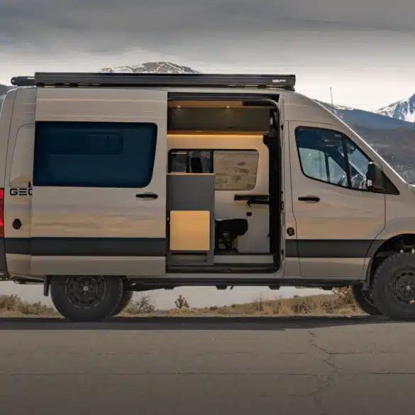 Geotrek Convoy Camper Van mit geöffneter Seitentür, Allradreifen und Dachträger vor einer verschneiten Berglandschaft