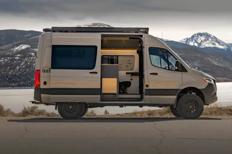 Geotrek Convoy Camper Van mit geöffneter Seitentür, Allradreifen und Dachträger vor einer verschneiten Berglandschaft